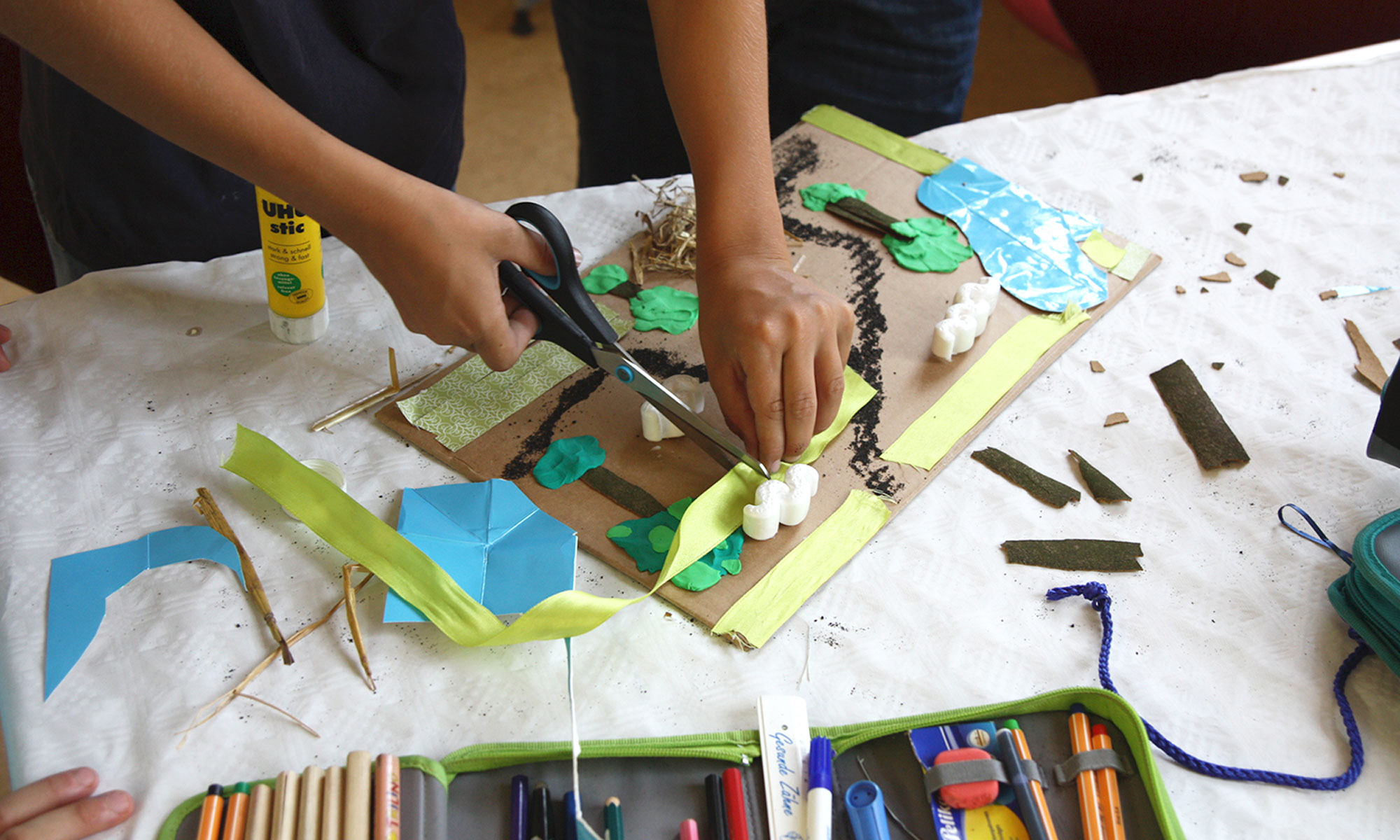 Materialbild aus Knete, Styropor, Bändern, Stroh und anderen Materialien, bearbeitet durch zwei Kinderhände